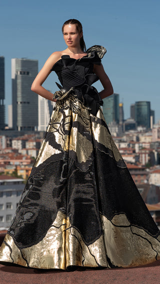 Woman in black and gold gown with city backdrop.