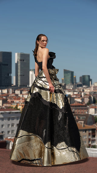 Woman in black and gold gown with city skyline background.