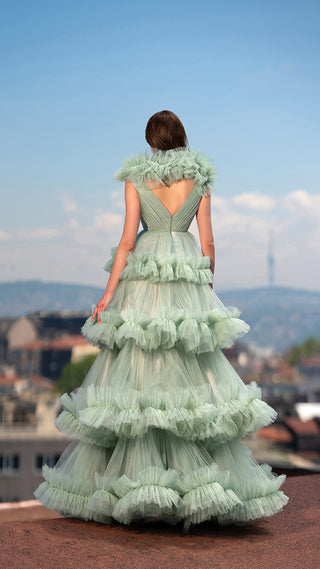 Woman in a tiered, ruffled green gown, back to the camera, outdoors.