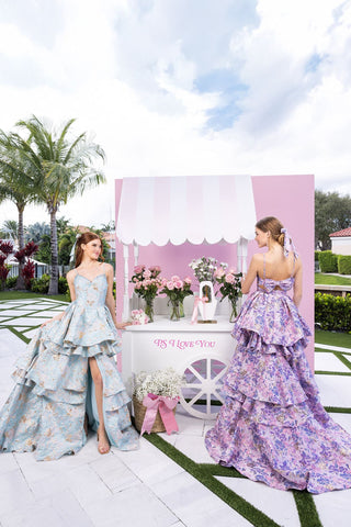 Two women in floral gowns by flower cart