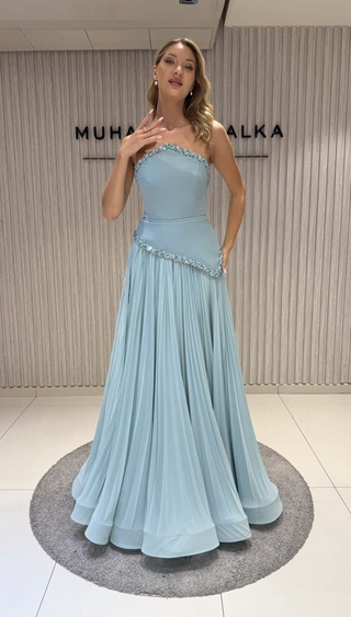 Woman in a light blue formal gown standing on a rug.