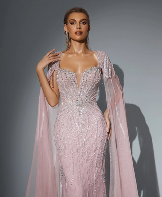 Woman in a pink, beaded gown with cape sleeves.