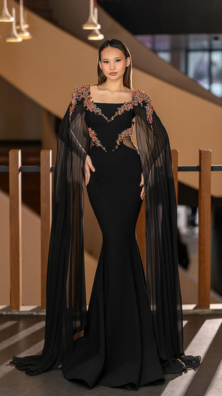 Woman in a black evening gown with cape sleeves.