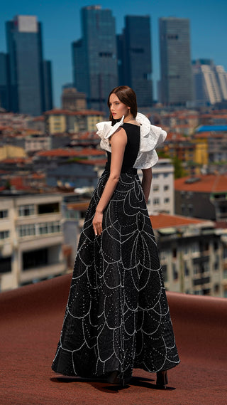 Woman in black and white gown, city skyline background.