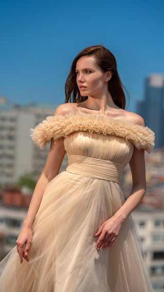 Woman in a beige off-shoulder gown, posing outdoors.