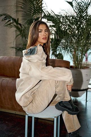 Woman in beige outfit sitting on a stool.