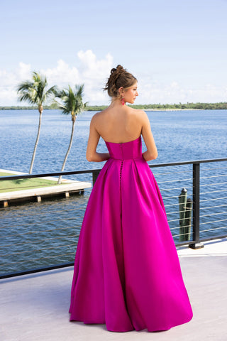 Magenta strapless gown by XO110 overlooking water.