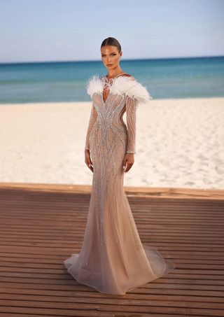 Woman in a long, beaded gown with feather accents, standing on a deck by the...